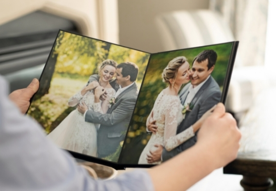 Photographer holding open a luxury photo album showing a wedding couple embracing outdoors