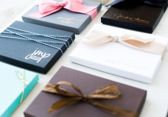 High-end branded photo delivery boxes in navy, white, and teal with satin ribbons and studio logo embossing