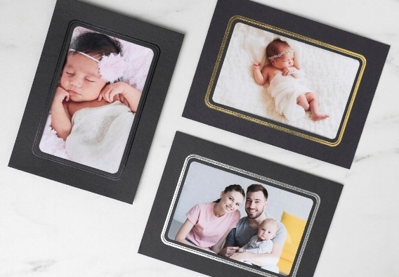 Professional photo folders and mounts displaying newborn and family portrait prints on a marble surface