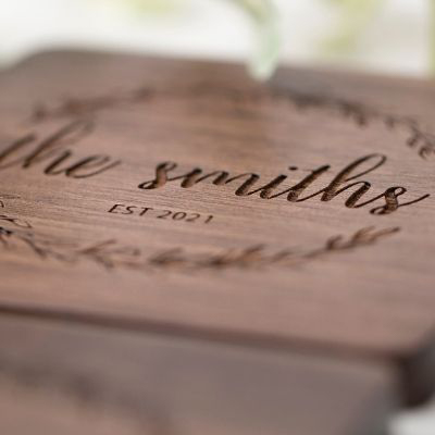 Close-up of laser engraved wood surface with cursive "The Smiths Est. 2021" family name and wreath design