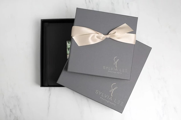 Slate album box at an angle with custom foil studio logo and champagne ribbon     Tyndell album packaging