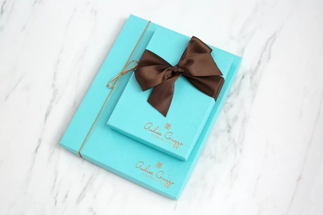  Two robin egg blue deluxe portrait boxes with custom foil studio logo and brown ribbon on marble surface     Tyndell