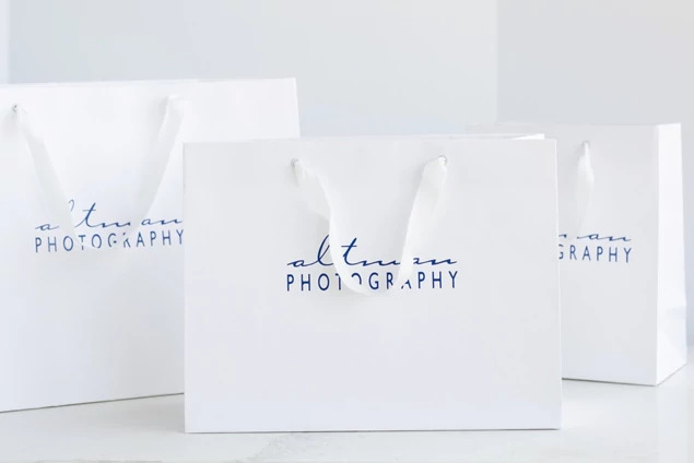 Two white Euro Tote bags shown flat view displaying foil imprinted studio branding on white finish