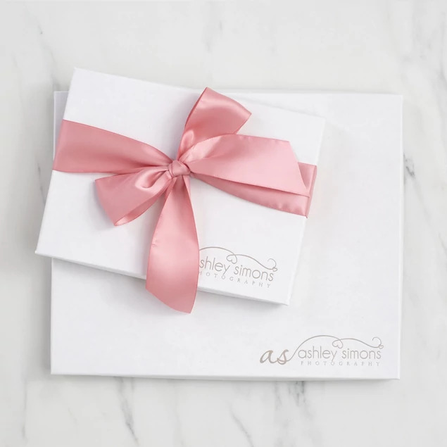 Matte white deluxe portrait box with custom foil studio logo and pink satin ribbon on marble surface     Tyndell
