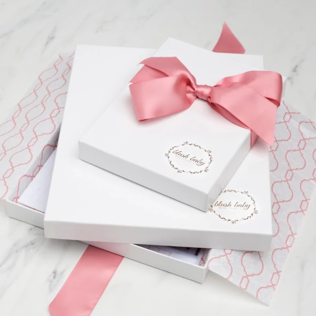 Two stacked white leather portrait boxes with custom foil studio logo and pink ribbon on patterned tissue paper     Tyndell