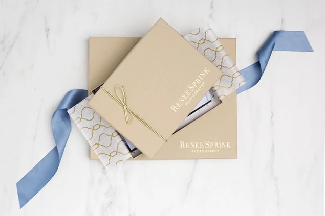  Open kraft portrait box with custom foil studio logo and blue ribbon on marble surface     Tyndell