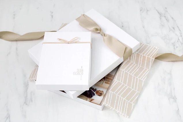 White leather portrait box open displaying portrait prints with champagne ribbon accent     Tyndell portrait box
