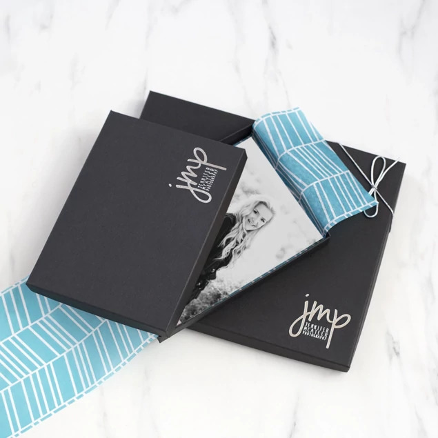 Open matte black deluxe portrait box with senior portrait print and teal patterned tissue paper     Tyndell