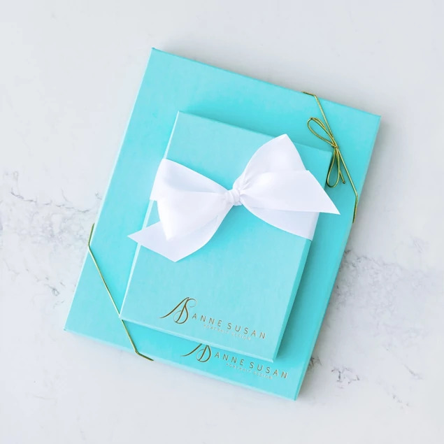 Two robin egg blue deluxe portrait boxes with custom gold foil studio logo and white ribbon on marble surface     Tyndell