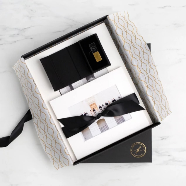 Open matte black presentation box displaying photo book and USB drive with custom foil logo     Tyndell presentation packaging