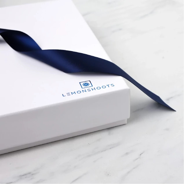 White soft touch album box closed with custom foil studio logo and navy ribbon on marble surface     Tyndell wedding album box