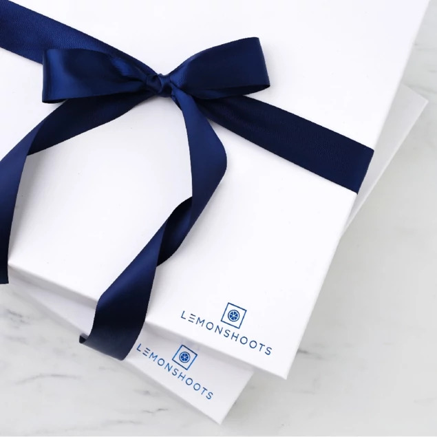 Two white soft touch album boxes with custom foil studio logo and navy satin ribbon on marble surface     Tyndell