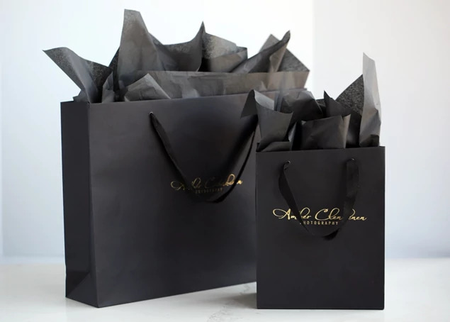 Two black Euro Tote bags with foil imprinted studio logo and tissue paper shown in two sizes