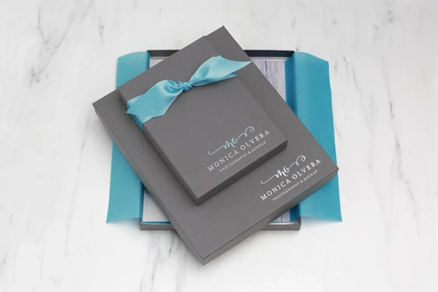Two slate portrait boxes with custom foil studio logo and teal ribbon on marble surface     Tyndell