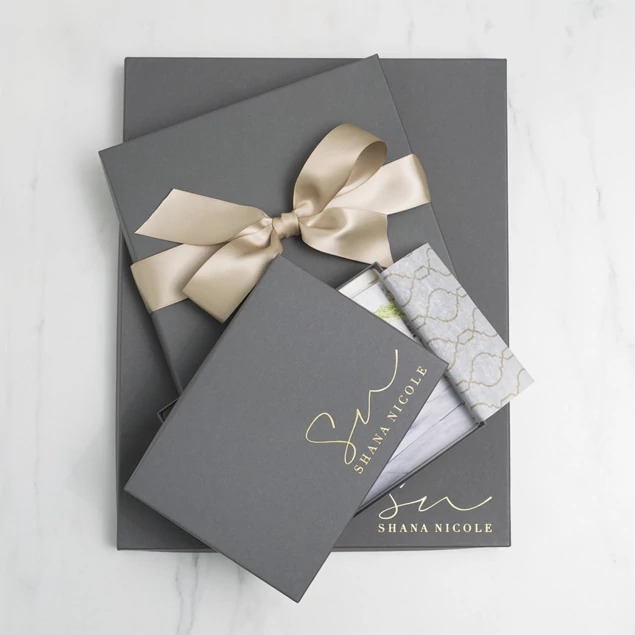 Slate portrait box with champagne ribbon and custom foil studio logo on marble surface     Tyndell