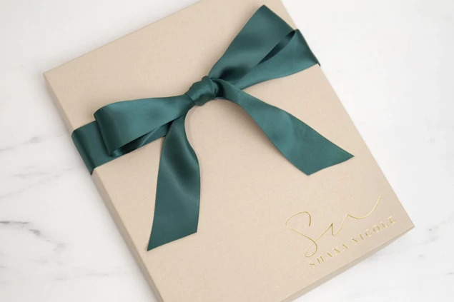 Kraft portrait box closed with green ribbon and custom foil studio logo on marble surface     Tyndell