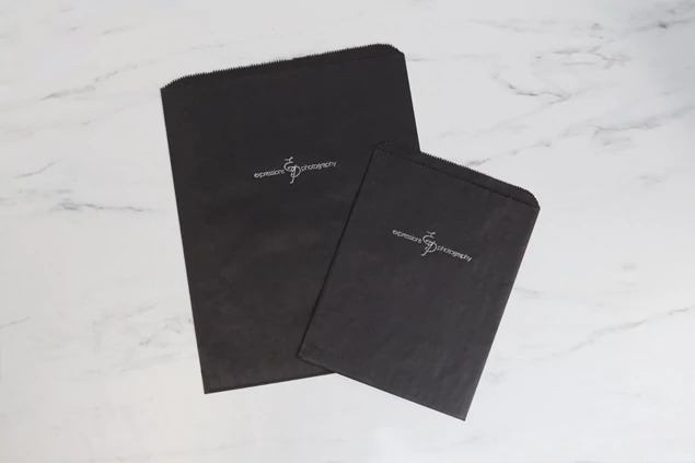 Black flat paper bags shown stacked displaying clean black paper construction and open top design