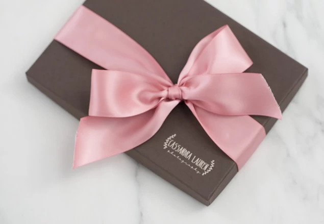  Close-up of matte chocolate deluxe portrait box with custom foil studio logo and pink satin ribbon     Tyndell