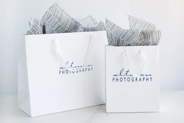 Two white Euro Tote bags with tissue paper and foil imprinted studio logo showing cotton twill handles