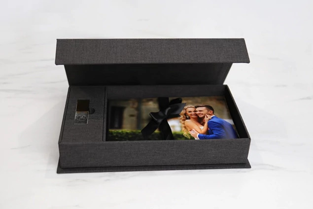 Carbon fabric flash and print box open showing USB insert and prints with satin ribbon closure