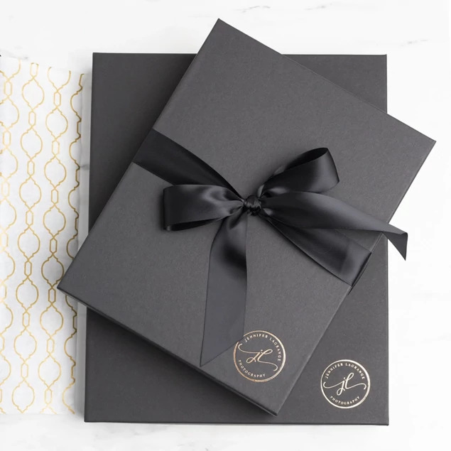 Matte black presentation box with custom foil studio logo and black satin ribbon on marble surface     Tyndell